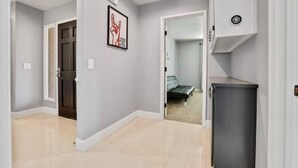 A hallway with a door leading to a bedroom, a framed picture on the wall, and a small cabinet.