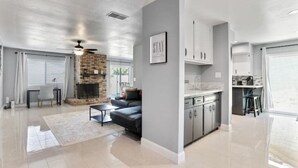 A modern living room with a fireplace, a sofa, and a dining area with a kitchen in the background.