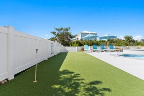 A pool area with artificial turf, lounge chairs, and umbrellas.