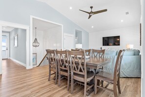 A dining area with a wooden table and chairs, a ceiling fan, and a TV mounted on the wall.