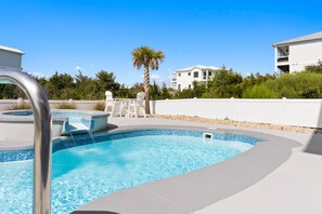 Een zwembad met een jacuzzi, ligbedden en een palmboom.