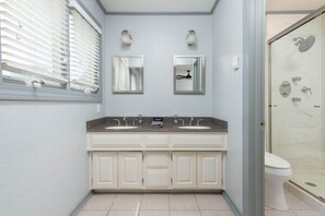 A bathroom with a double sink vanity, a toilet, and a glass shower enclosure.