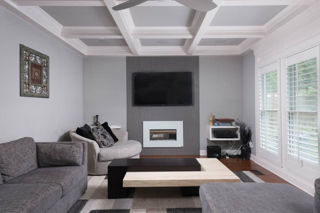Een moderne woonkamer met een open haard, grijze banken en een flatscreen televisie aan de muur.