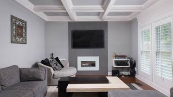 Een moderne woonkamer met een open haard, grijze banken en een flatscreen televisie aan de muur.