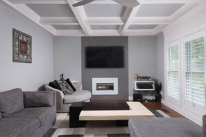 A modern living room with a fireplace, grey sofas, and a flat-screen TV mounted on the wall.