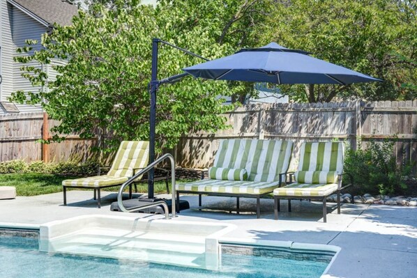 A backyard with a swimming pool, two lounge chairs, and a blue umbrella. - Luxury in Lenexa w/heated pool (Lenexa)