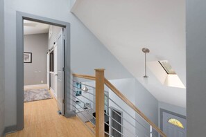 A modern staircase with a wooden handrail and metal balusters, leading to a lofted area with a skylight. - Luxury in Lenexa w/heated pool (Lenexa)