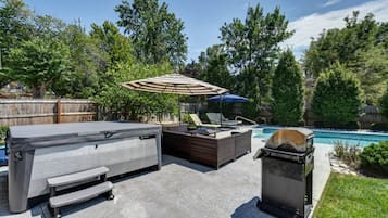 A backyard with a hot tub, outdoor seating, and a grill.