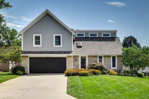 A two-story house with a garage, stone facade, and a well-maintained lawn. - Luxury in Lenexa w/heated pool (Lenexa)