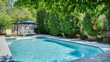 A rectangular swimming pool with clear blue water, surrounded by a concrete deck and a wooden fence.