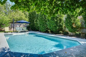 Una piscina rettangolare con acqua cristallina e blu, circondata da un solarium in cemento e una recinzione in legno.