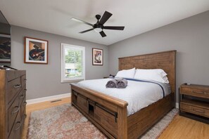 Una camera da letto con un letto di legno, una ventola a soffitto, una finestra e opere d'arte alle pareti.