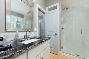 A modern bathroom with a marble sink, a large mirror, and a glass shower enclosure.