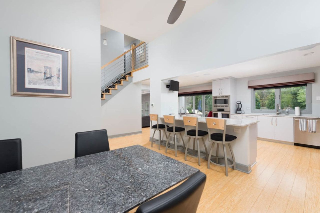 Een moderne keuken met een centraal eiland, barkrukken en een trap naar een hoger gelegen verdieping.