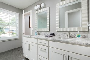 A modern bathroom with two sinks, a large mirror, and a window with blinds. - Luxury in Lenexa w/heated pool (Lenexa)