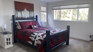 A bedroom with a bed, nightstand, lamp, and a window with a view of trees.