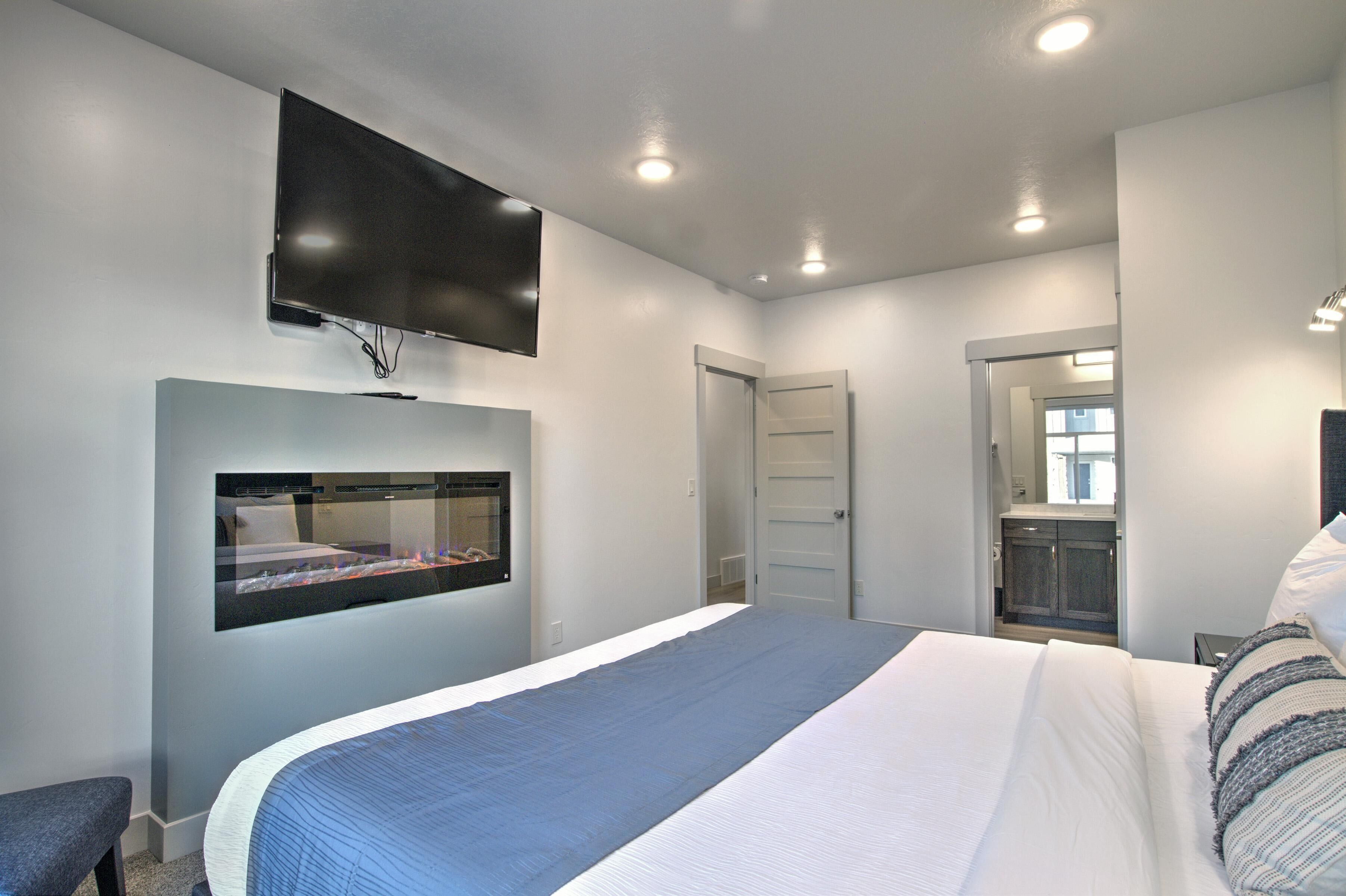 A modern bedroom with a large bed, a mounted TV, and a built-in aquarium.