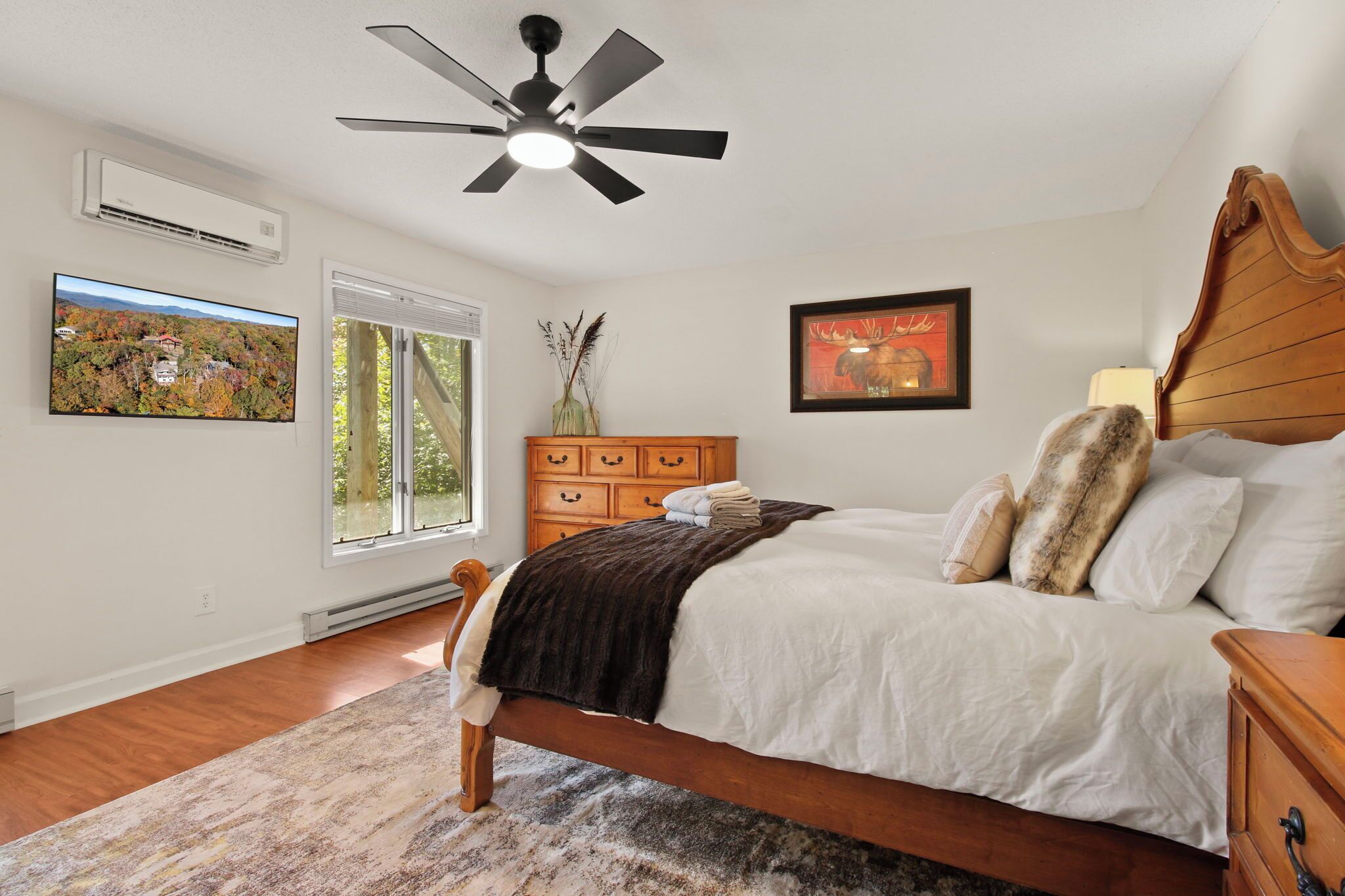 Une chambre à coucher comprenant un lit, une commode en bois, un ventilateur de plafond, une fenêtre et un climatiseur fixé au mur.
