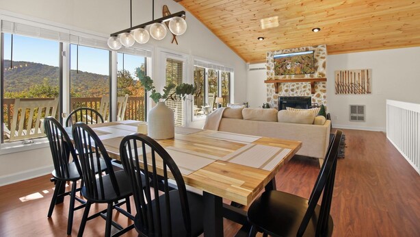Un comedor amplio con una mesa de madera, sillas negras y un ventanal que ofrece vistas a un paisaje montañoso.