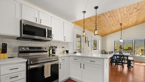 Una cocina moderna con armarios blancos, electrodomésticos de acero inoxidable y techo de madera.