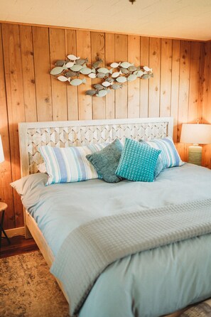 Una cama con cabecera de madera, varios almohadones y un adorno de pez colgado en la pared.