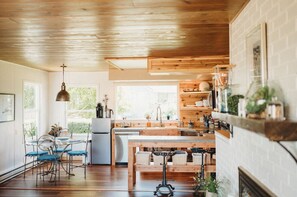 A kitchen with wooden cabinets, a dining table with blue chairs, and a hanging light fixture. - 1- Cheerful and cozy water-view cottage (sequim)