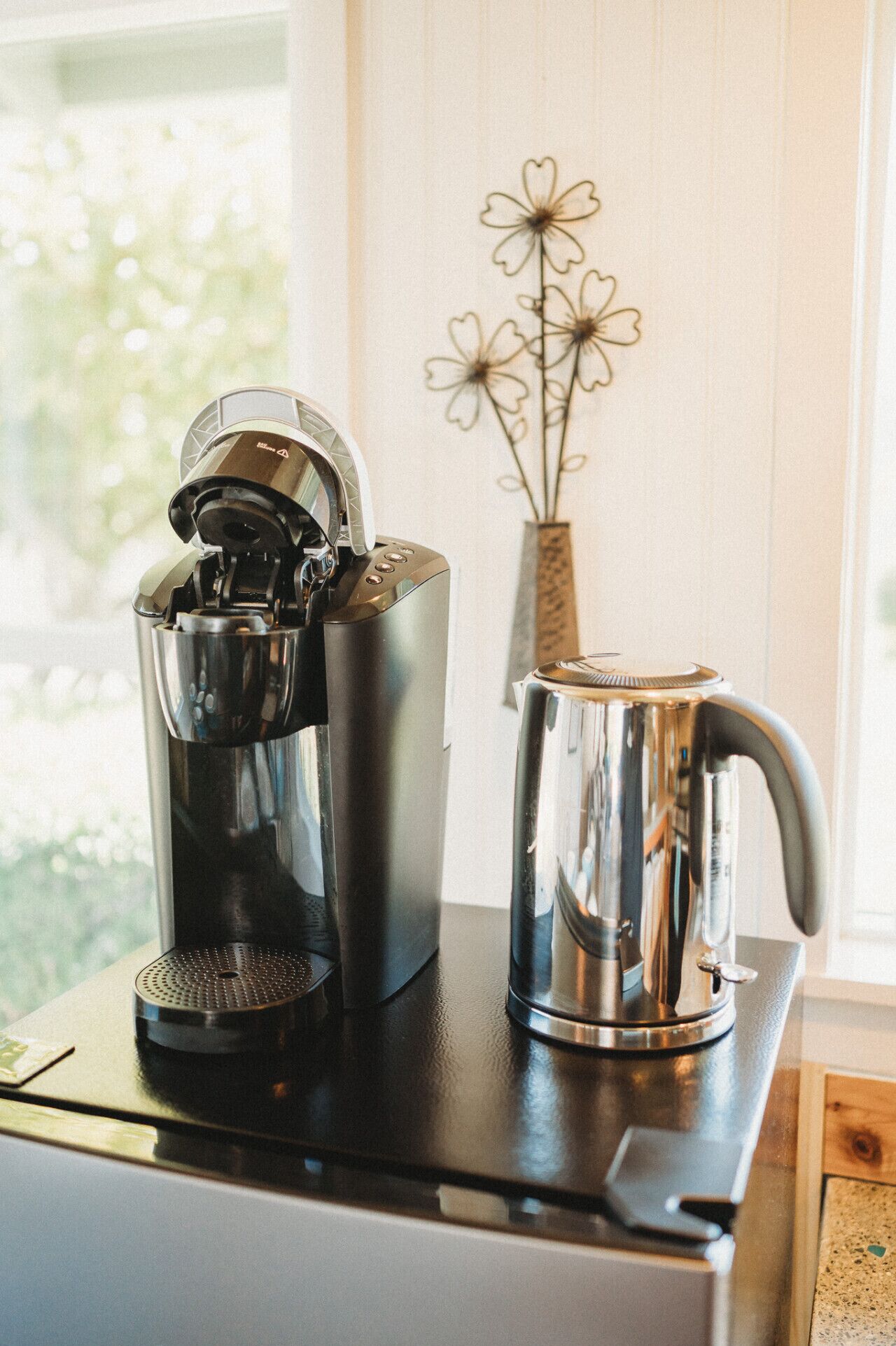 Eine Kaffeemaschine, ein Wasserkocher und eine Tasse auf einer Arbeitsplatte in der Nähe eines Fensters.