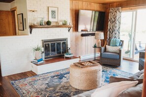 A cozy living room with a fireplace, a television, wicker furniture, and a patterned rug. - 1- Cheerful and cozy water-view cottage (sequim)