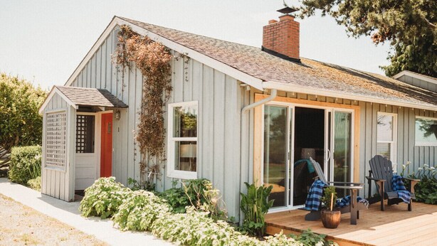 Una casa pequeña de un piso con terraza de madera, puerta corredera de vidrio y puerta roja.
