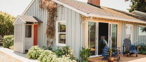 Una casa pequeña de un piso con terraza de madera, puerta corredera de vidrio y puerta roja.