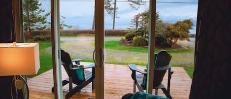 A room with a view through a sliding glass door to an outdoor deck with two chairs and a table.