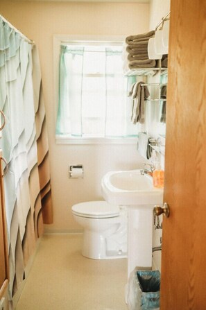 Un baño pequeño con inodoro, lavamanos y una ventana con cortinas.