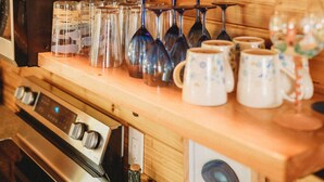 Una cocina con estantes de madera que exhiben diversos utensilios, incluyendo cristalería y tazas.