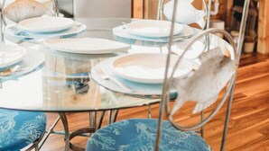 Un comedor con mesa de vidrio, sillas de metal con cojines azules y una lámpara colgante.