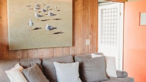 Una sala de estar acogedora con un sofá gris, un tapete colorido y un cuadro grande de pájaros en la pared.