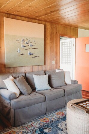 A cozy living room with a grey sofa, a colorful rug, and a large painting of birds on the wall.