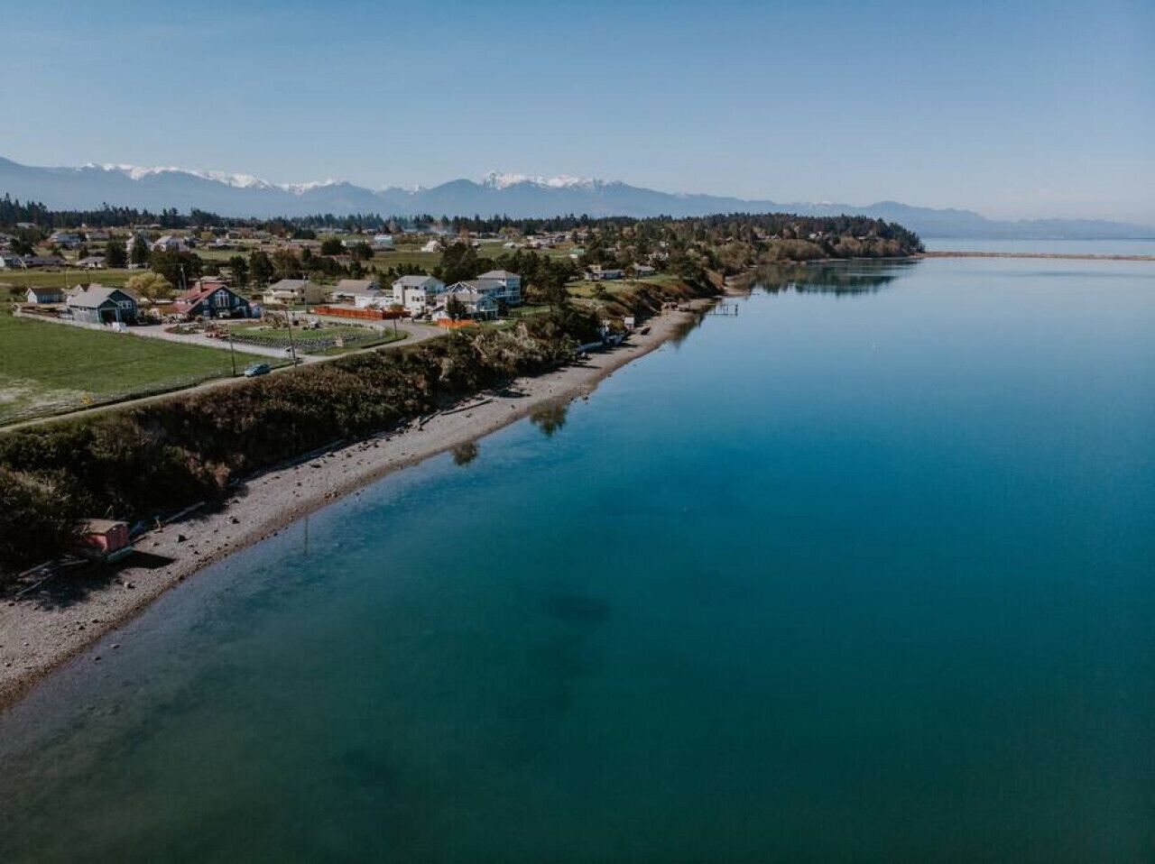 A coastal town with houses along a riverbank, a clear sky, and distant mountains.