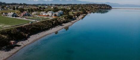 A coastal town with houses along a riverbank, a clear sky, and distant mountains.