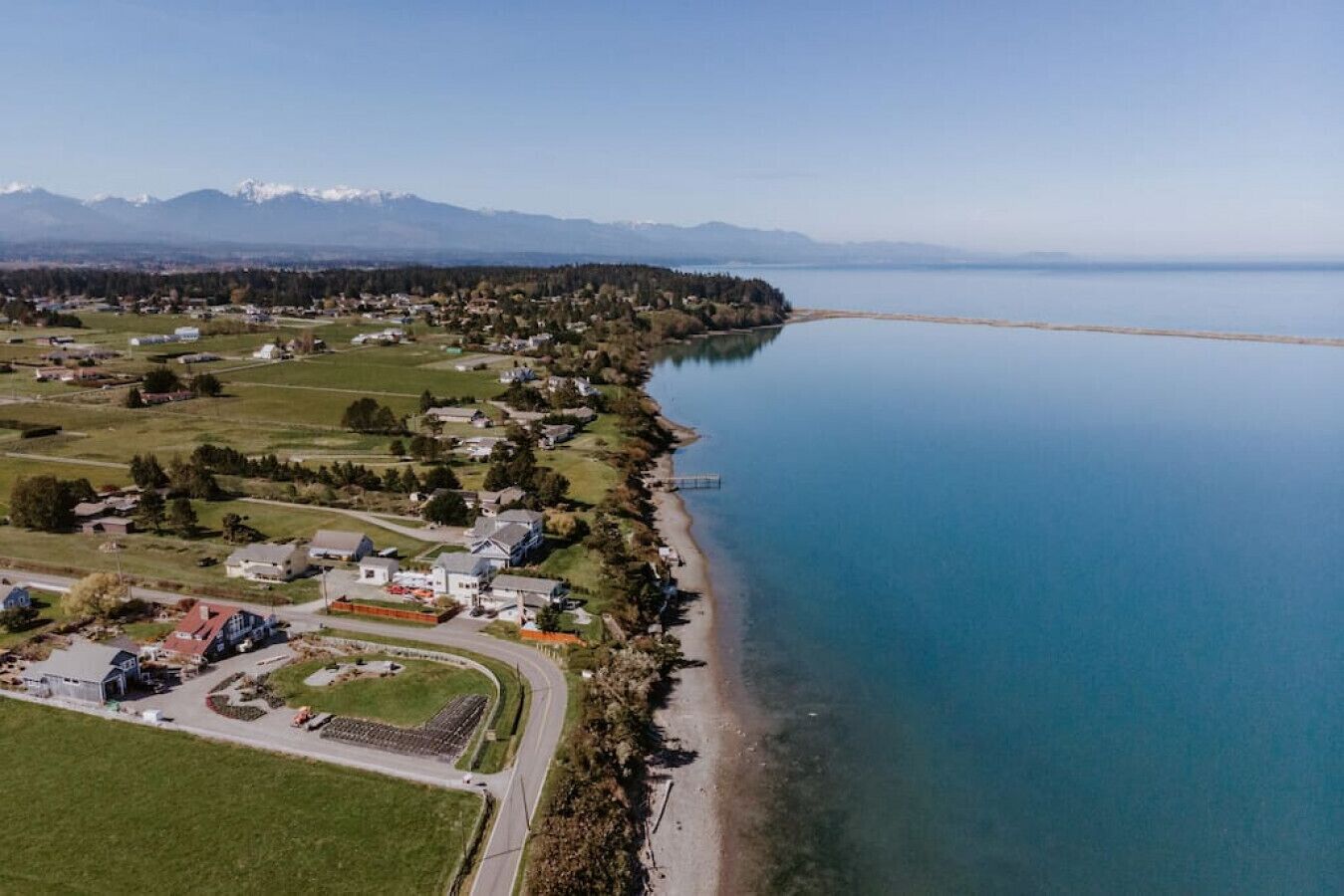 Vista aérea de uma comunidade à beira de um lago, com edifícios residenciais, um cais e uma estrada que leva à margem.