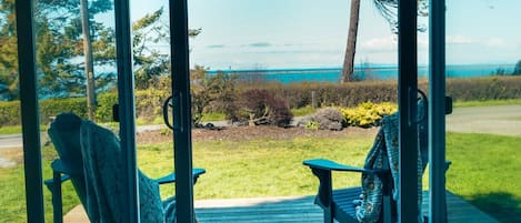 A deck with two Adirondack chairs facing a grassy area and a view of the ocean.