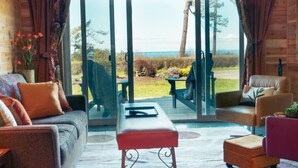 Ein modernes Wohnzimmer mit einer Couch, Sesseln und einem Couchtisch. Es verfügt über große Glasüren, die auf eine Terrasse mit Blick aufs Meer führen.