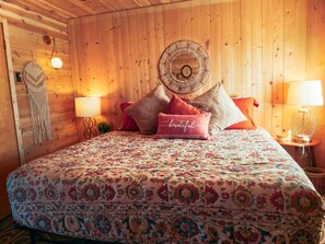 A wooden room with a bed, two lamps, and a wall hanging.