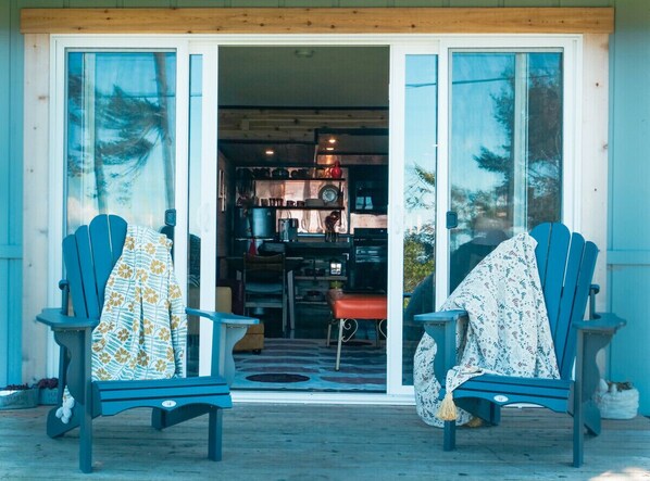 A wooden deck with two blue Adirondack chairs, one with a floral blanket and the other with a white blanket.