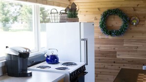 A compact kitchen with a white refrigerator, a blue kettle, and a wooden wall with a wreath. - Rm 4 Sequim lavender · 4-Water View-Beach access-Sequim's Lavender Room (Sequim)