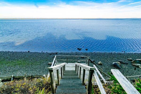 A wooden staircase leading to a rocky shoreline with a view of the ocean.