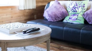 A living room with a dark leather sofa, purple and green patterned pillows, a wooden coffee table with a board game and remote controls. - Rm 4 Sequim lavender · 4-Water View-Beach access-Sequim's Lavender Room (Sequim)