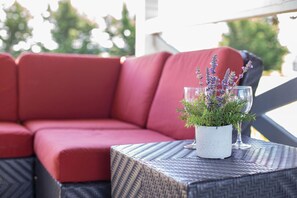 A red cushioned outdoor seating area with a woven table and a potted plant with purple flowers. - Rm 4 Sequim lavender · 4-Water View-Beach access-Sequim's Lavender Room (Sequim)
