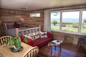 Una cabaña acogedora con una cama, un sofá rojo, una mesa de comedor y vistas al mar.