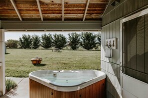 Un bain à remous situé dans un espace extérieur abrité, doté d’un plafond en bois, d’une pelouse et d’une clôture en bois.