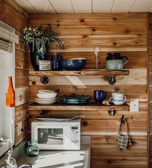 Una cocina con paredes de madera, un microondas, una cafetera y diversos platos y utensilios.